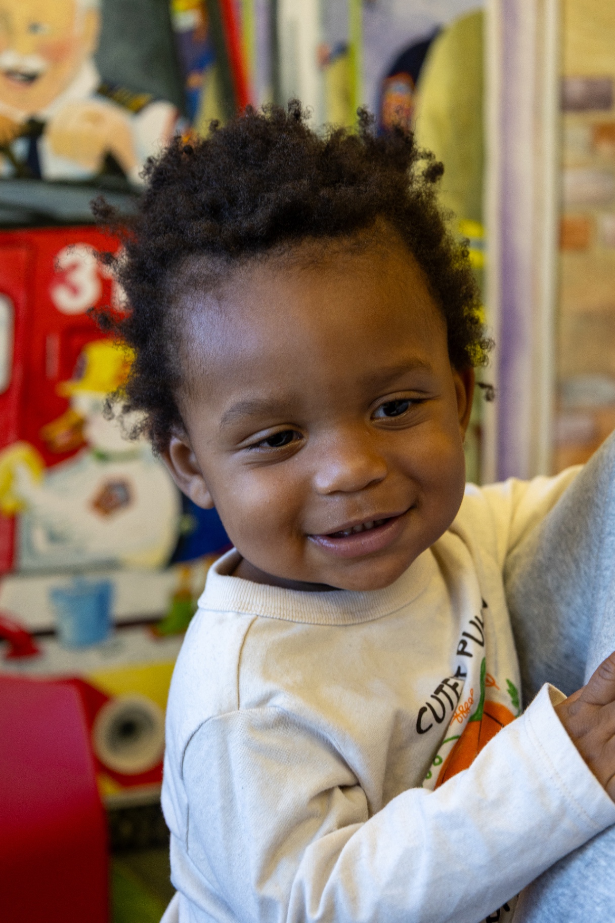 Close-up of a smiling toddler in an examination room with a fire truck mural behind