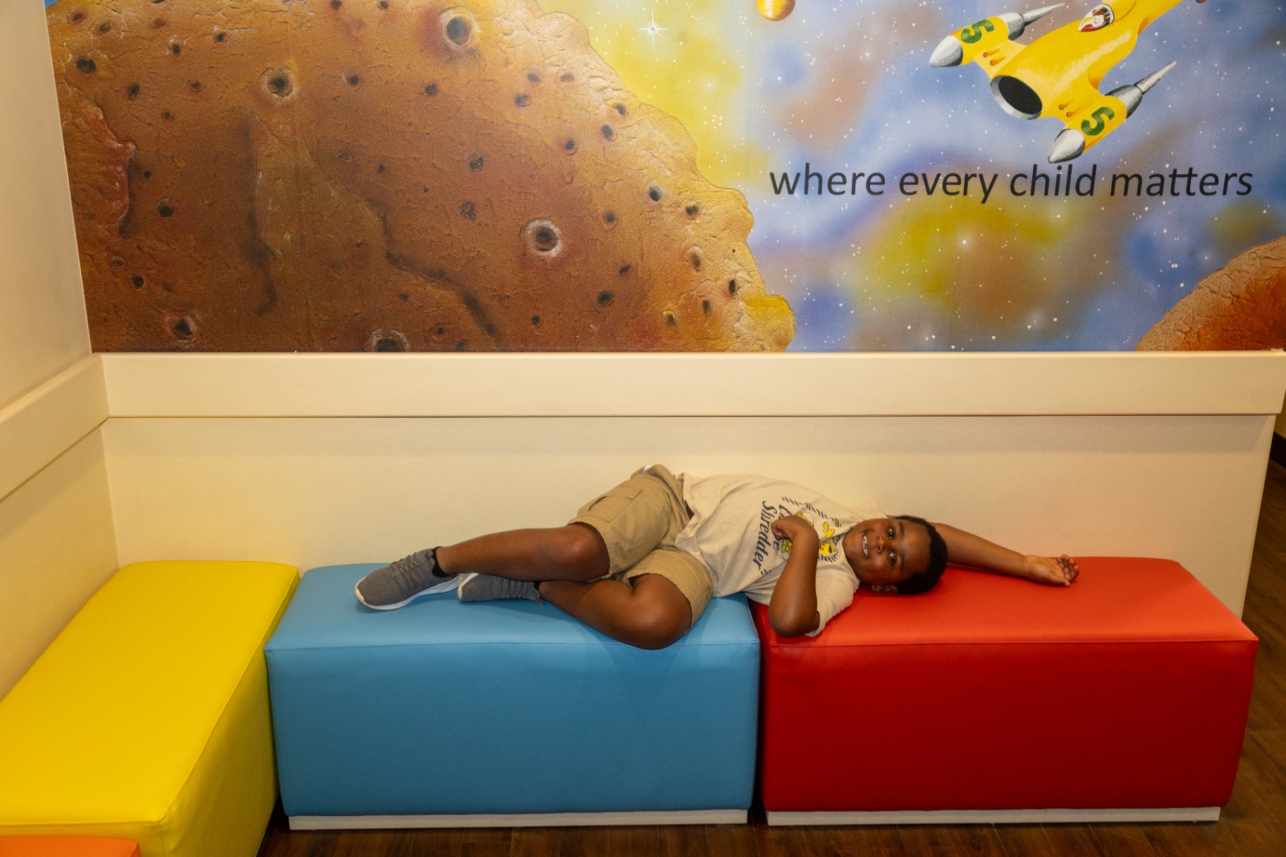 A child lying comfortably across the waiting room benches under the space mural
