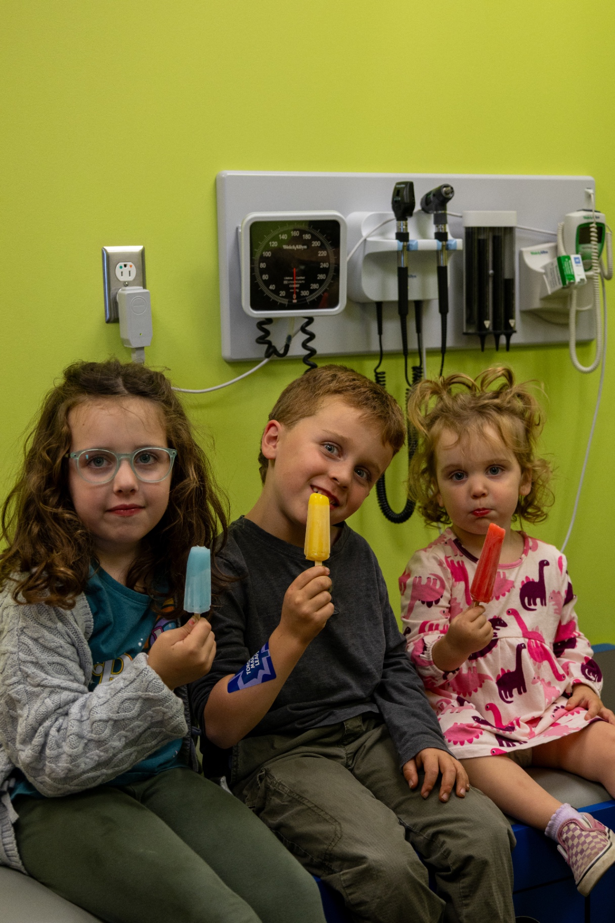Three children holding colourful freezies beside an exam room wall unit