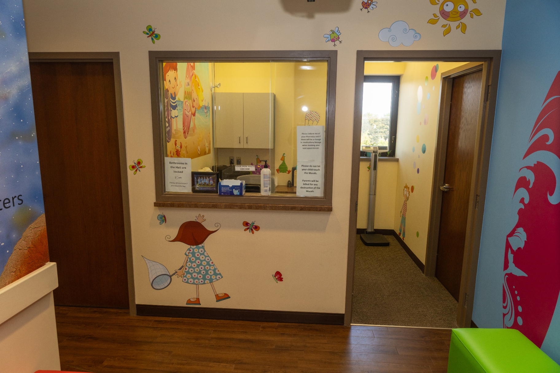 Reception window with cheerful wall decals and a hallway leading to the examination rooms