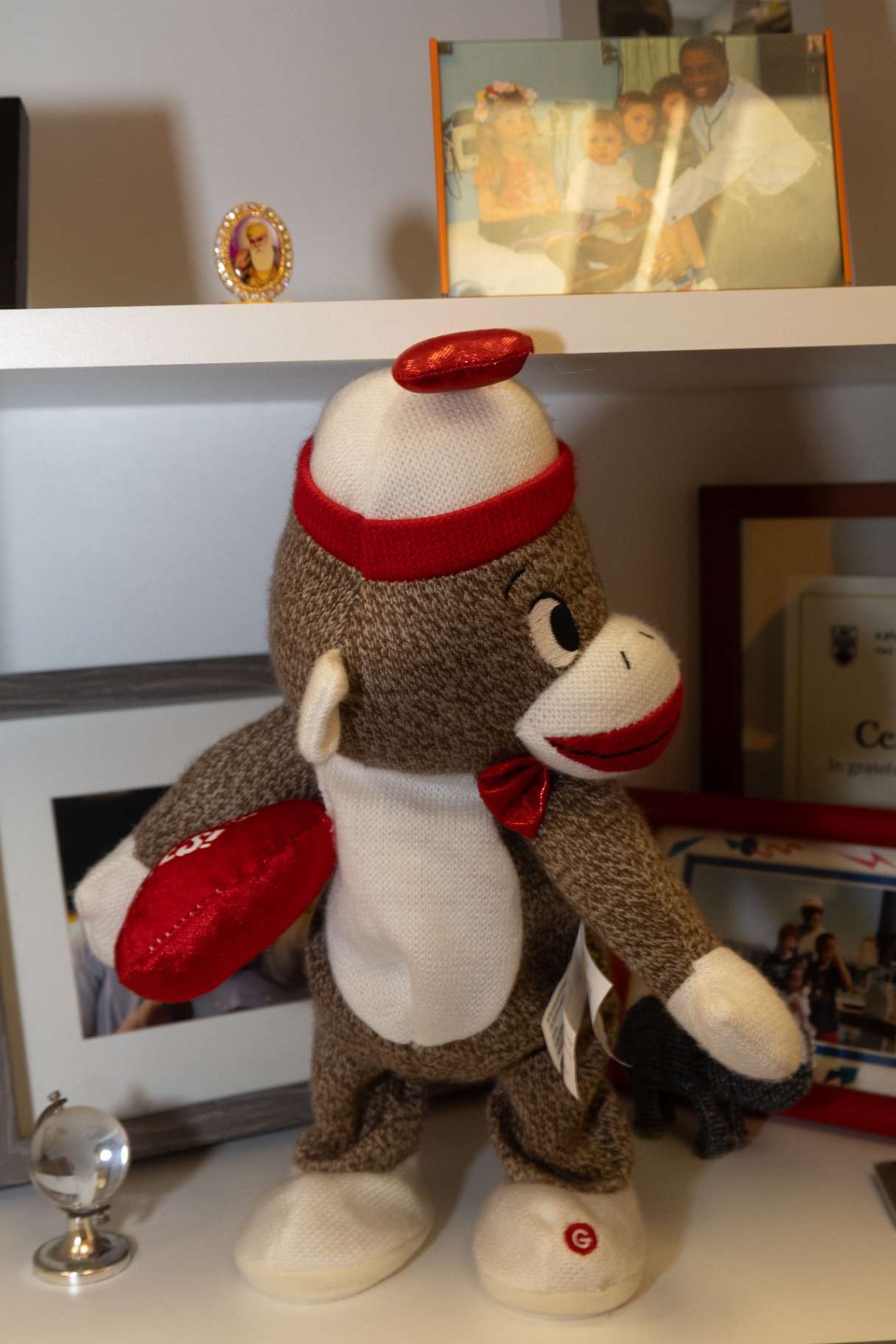 Knitted sock monkey toy on a shelf beside framed family photographs