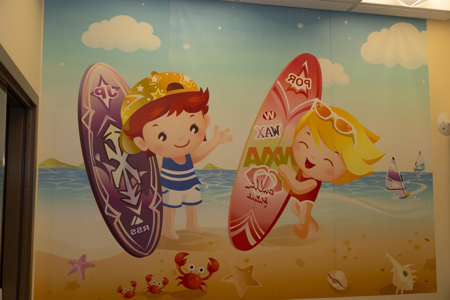 Wall mural of two children holding surfboards at the beach